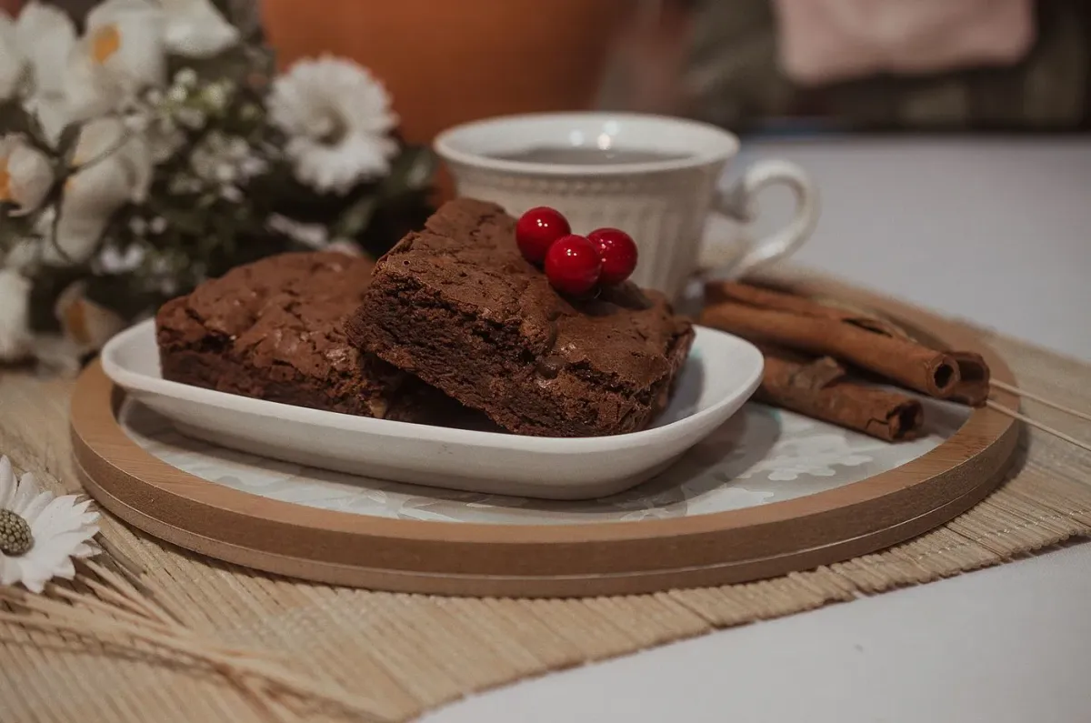 Dois pedaços de brownie de chocolate com cerejas, ao lado de uma xícara
