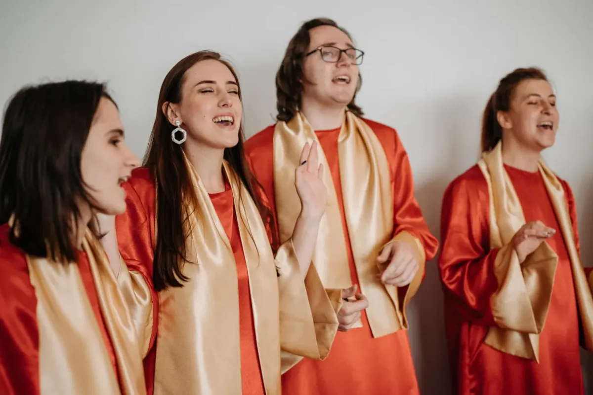 Quatro coralistas com túnicas vermelhas e echarpes douradas cantam de olhos fechados (imagem de arquivo, não é do Cantus Firmus)