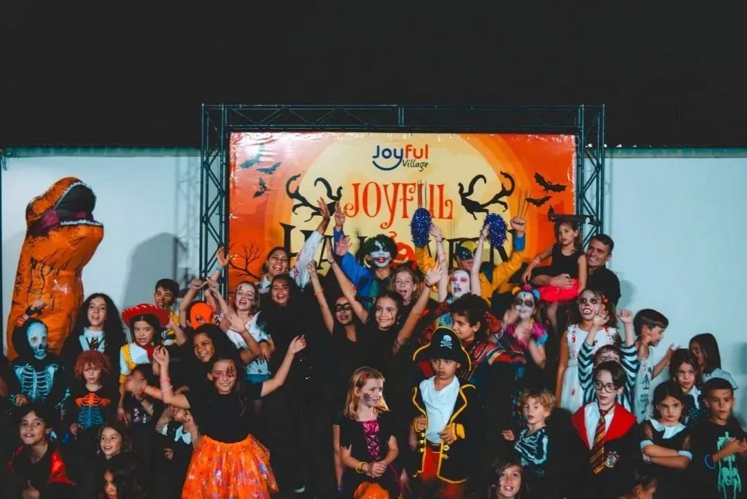 Crianças fantasiadas de bruxas, piratas e caveiras comemoram diante do painel do Joyful Halloween