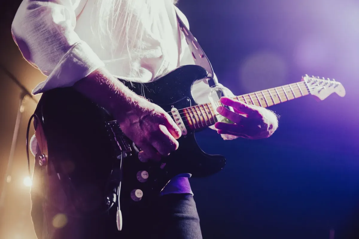 Mãos de guitarrista tocando guitarra elétrica sob luz roxa no palco (foto de banco de imagens)