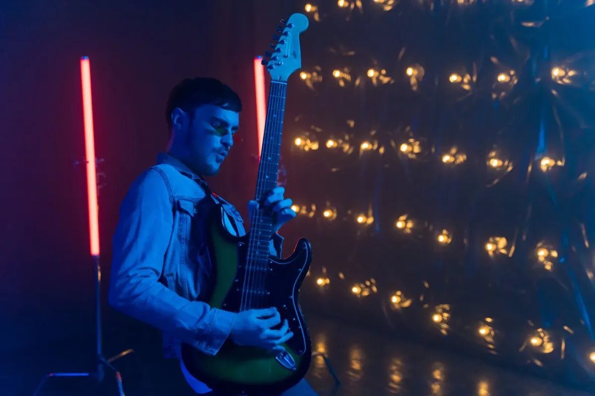 Guitarrista toca guitarra elétrica sob luzes azuis e vermelhas em palco (foto ilustrativa)