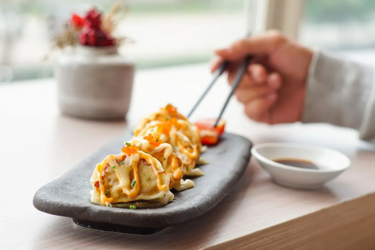 Gyozas com molho e ovas sobre prato de pedra, com hashis e molheira ao lado (imagem ilustrativa de banco, não é do restaurante)