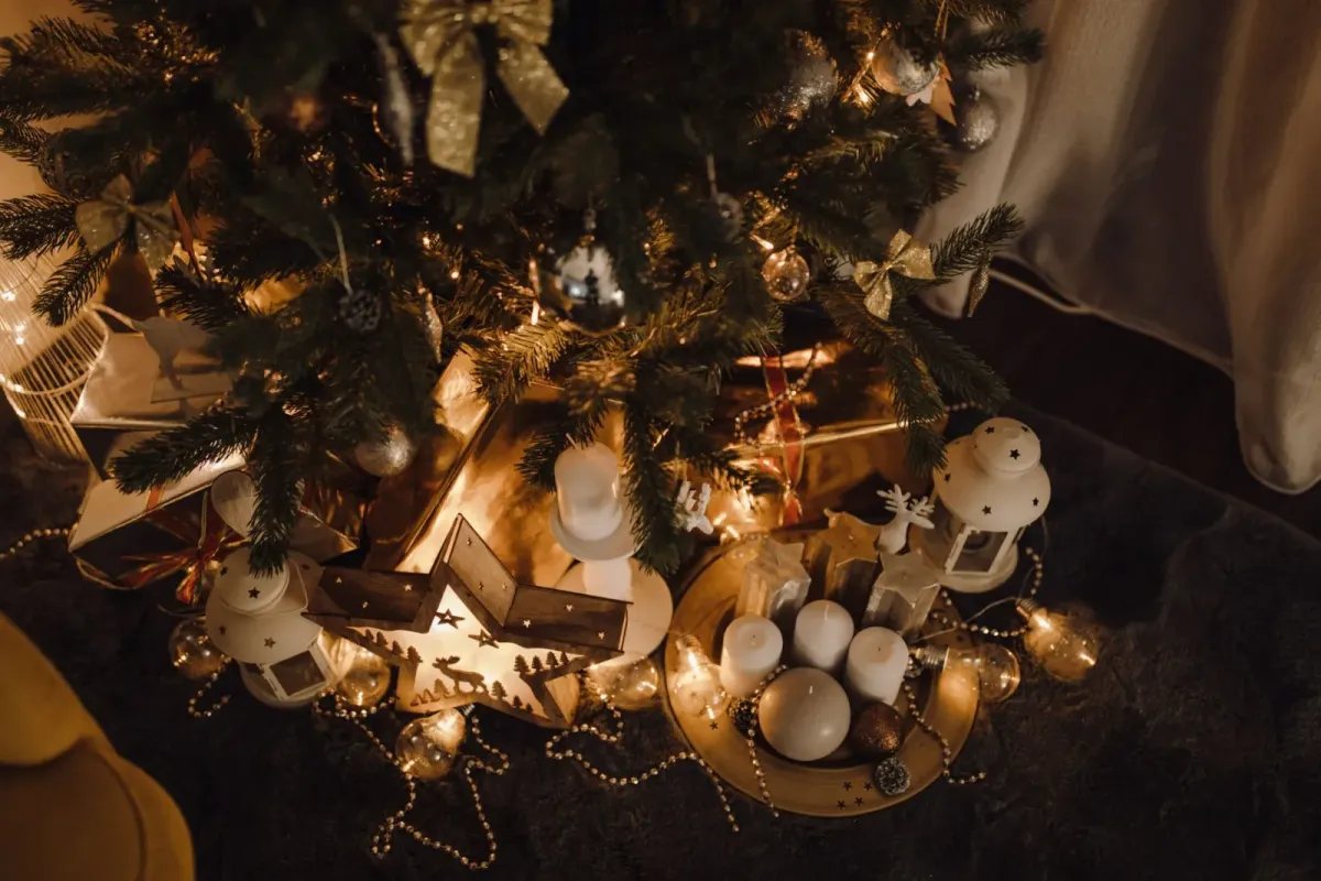 Pé de uma árvore de Natal com presentes, lanternas, velas e luzes acesas