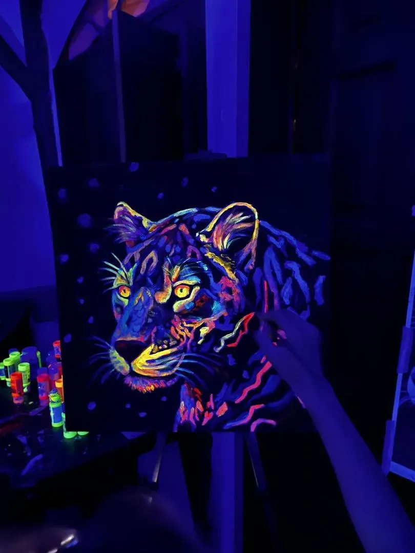 Tela pintada com tinta fluorescente mostrando uma onça colorida brilhando sob luz negra