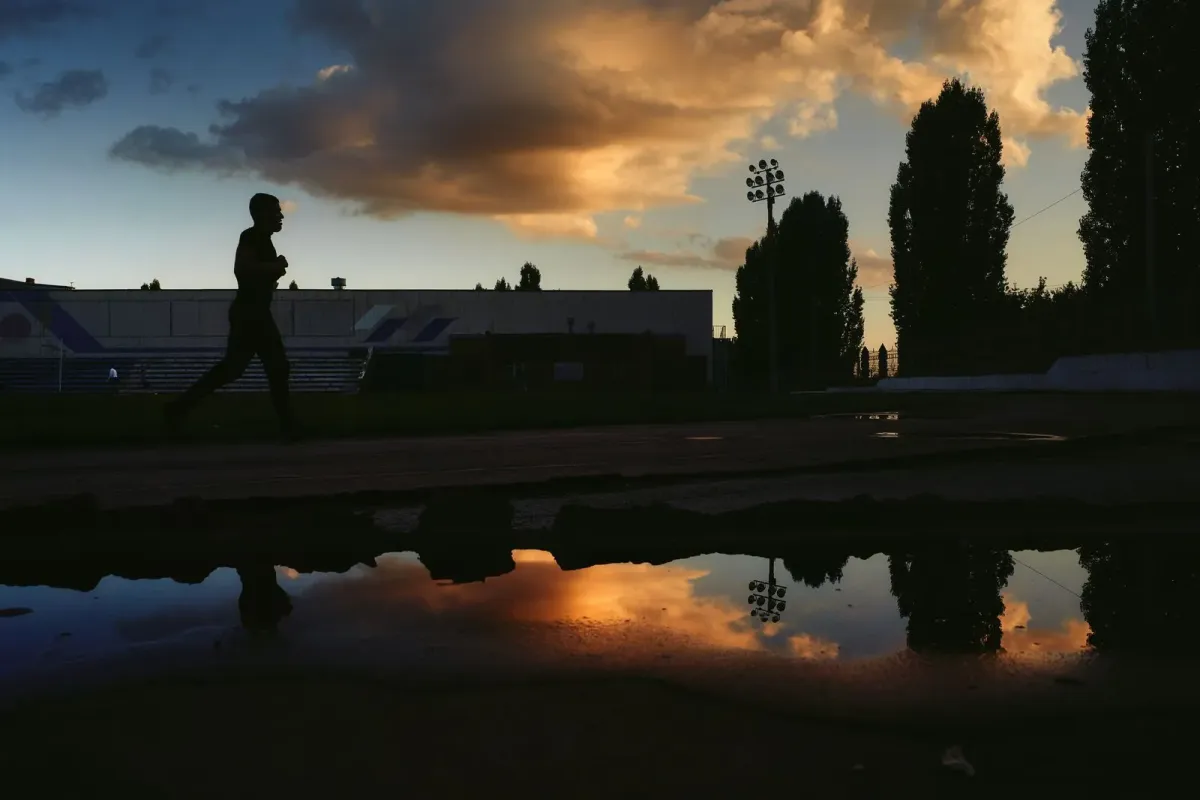Silhueta de um corredor numa pista de atletismo ao entardecer, com céu alaranjado refletido numa poça