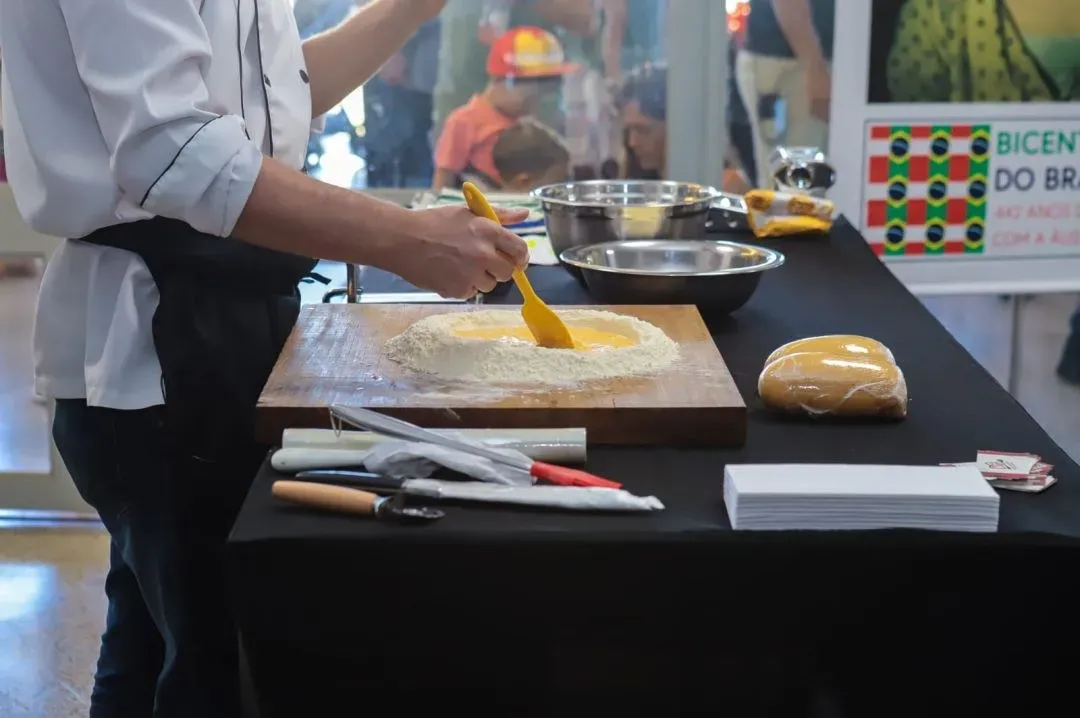 Chef prepara massa fresca sobre tábua de madeira, com farinha e ovos, em oficina de gastronomia italiana
