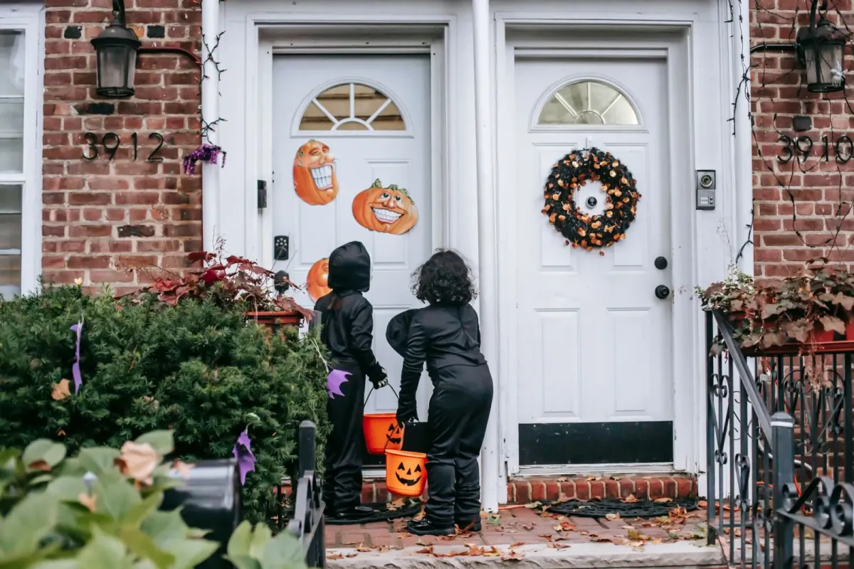 Crianças fantasiadas com baldes de abóbora pedem doces numa porta decorada