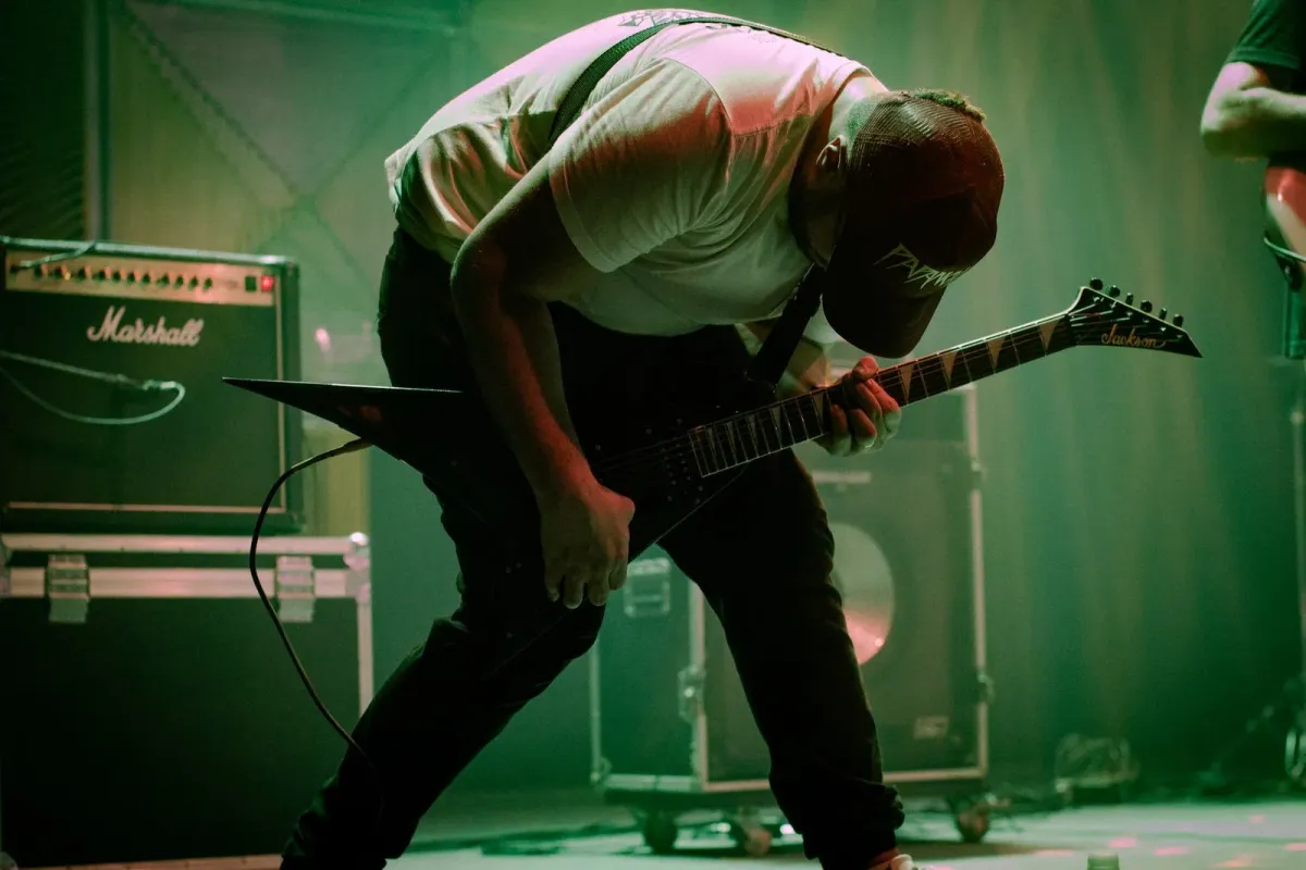 Guitarrista curvado sobre a guitarra em palco de show de rock com luz verde e vermelha