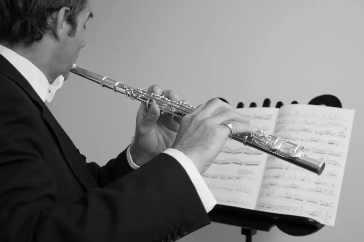 Flautista de terno toca flauta transversal diante da partitura, em foto em preto e branco