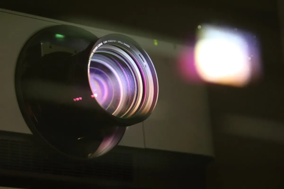Lente de um projetor de cinema emitindo um feixe de luz em ambiente escuro