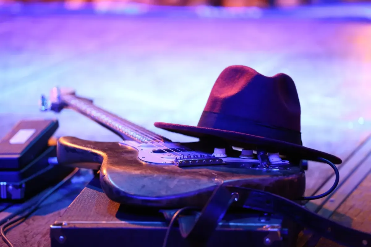 Guitarra elétrica e chapéu bordô sobre um amplificador em palco com luz azul e roxa, em foto de arquivo ilustrativa