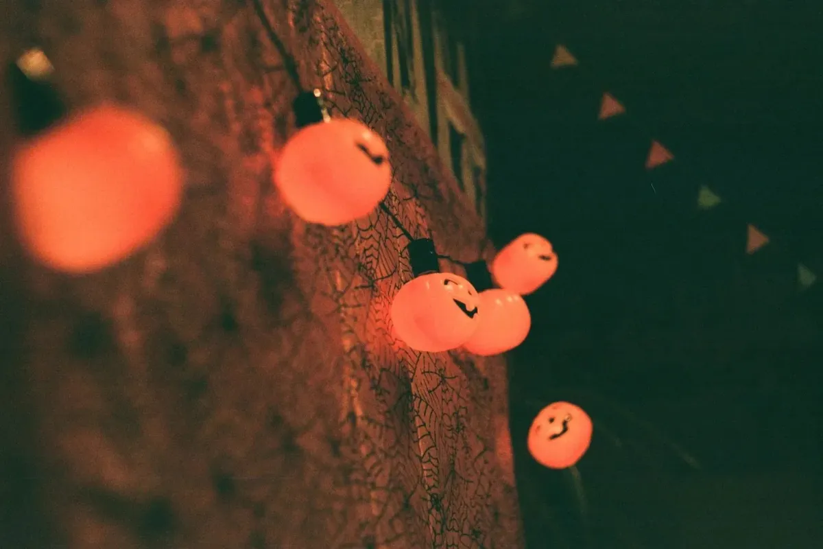 Luminárias em forma de abóbora de Halloween acesas, penduradas em parede com teia de aranha decorativa