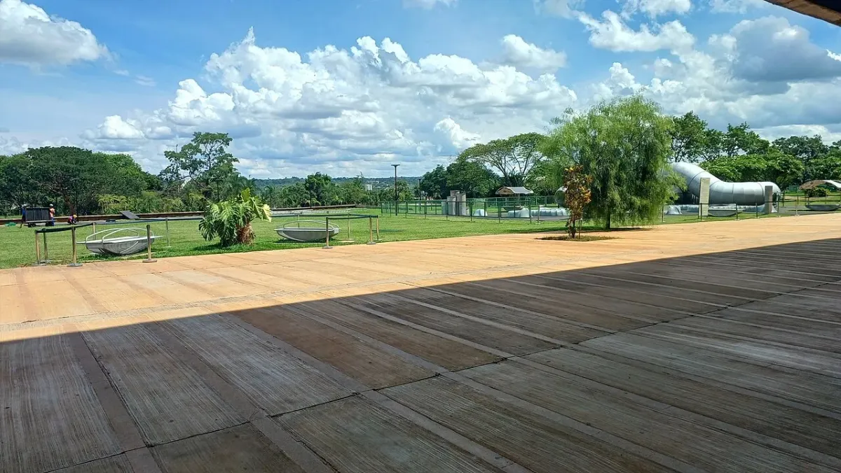 Piso de madeira e gramado nos jardins do CCBB Brasília, com árvores e estruturas ao fundo